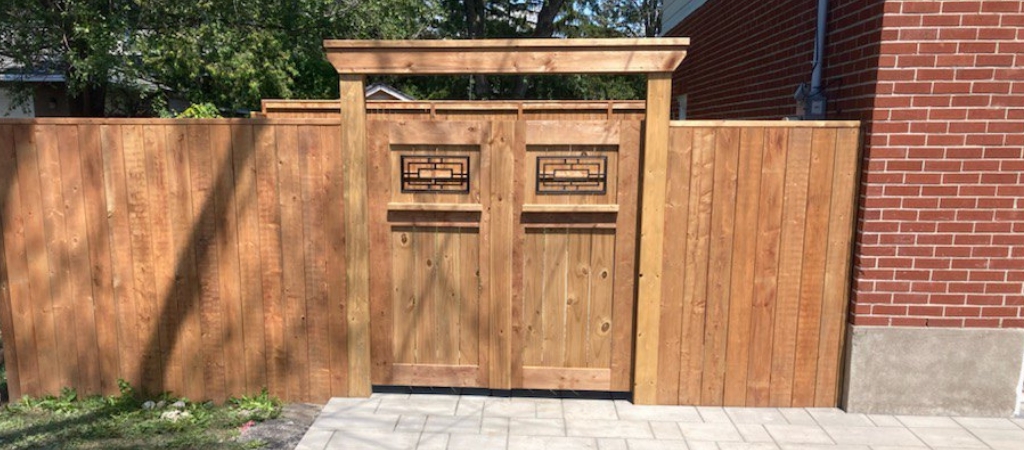 Exterior shot of a fence with craftsman style double-doors featuring an iron insert.